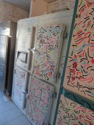 des réfrigérateurs et des congélateurs couverts de graffitis dans une cuisine au sol carrelé de blanc