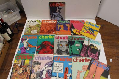 de nombreux livres posés sur une table, avec une bouteille de vin en arrière-plan