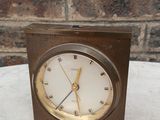 une petite horloge posée sur une table, avec un mur de briques en arrière-plan