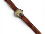 gros plan d'une montre sur une surface blanche avec un bracelet marron