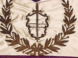 a white vest with a purple ribbon and a cross on it