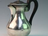 an antique silver coffee pot with a black handle on a white surface