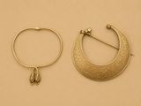 deux bijoux en or posés sur une surface beige