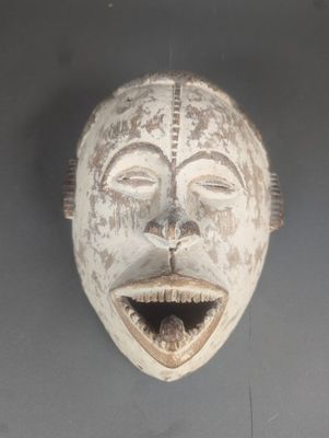 un masque en bois accroché au mur, sur lequel se dessine un sourire