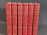 six red books lined up in a row on a gray surface
