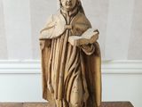 statue en bois représentant un homme tenant un livre posé sur une table en bois