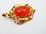 une image représentant une broche rouge et dorée ornée de perles