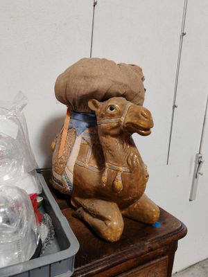 une statue représentant un chameau assis sur une table, à côté d'un récipient en plastique