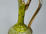 a green glass vase with a gold handle on a table