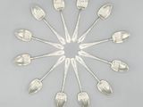 six cuillères en argent disposées en cercle sur une surface grise