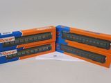 trois boîtes contenant des trains miniatures, posées sur une surface blanche