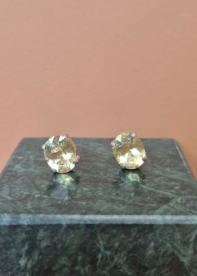 une paire de boucles d'oreilles à clous plaquées or, posées sur un socle en marbre
