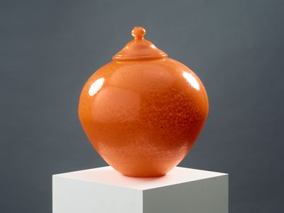un vase orange posé sur un socle blanc