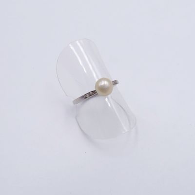 une bague en perle blanche et argent posée sur un verre transparent