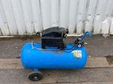 a blue air compressor sitting on the ground next to a white wall