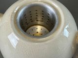 a white tea pot with a strainer inside of it