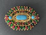 a close up of a broochle with a blue stone surrounded by green and red beads