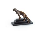 La statue en bronze représentant un chien est posée sur un socle noir.