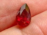 un diamant rouge en forme de larme au doigt d'une personne