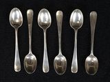six cuillères en argent sont alignées sur une surface noire
