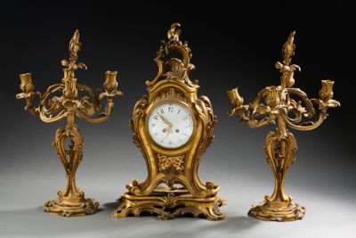 trois bougeoirs dorés et une horloge posés sur une table