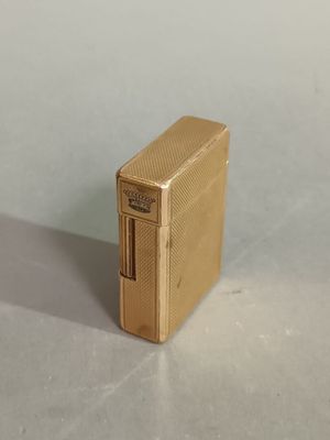 a gold lighter sitting on a table with a white wall behind it