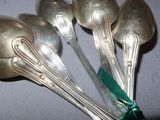 four silver spoons with green ribbon tied to them sitting on a table