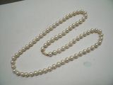 un collier de perles blanches muni d'un fermoir en or, posé sur une table