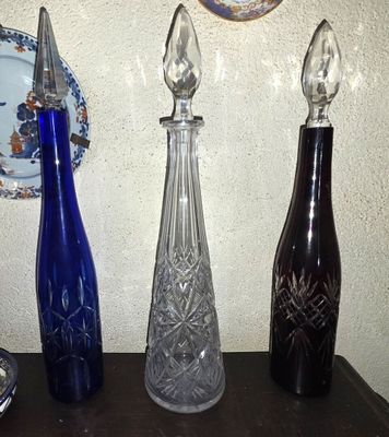 trois vases en verre posés sur une table où se trouvent également des assiettes et une horloge