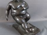statue d'un homme corpulent assis sur une assiette, sur fond gris