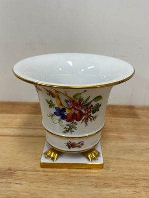 a small white vase with a gold rim on a wooden table