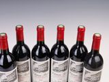 six bottles of red wine lined up in a row on a white surface