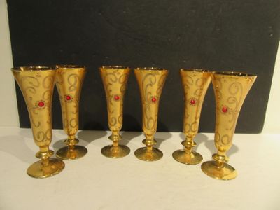 four gold wine glasses with red stones on them sitting on a table