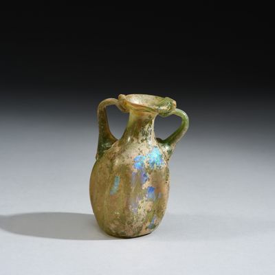 un vase vert et bleu muni d'une anse, posé sur une surface blanche