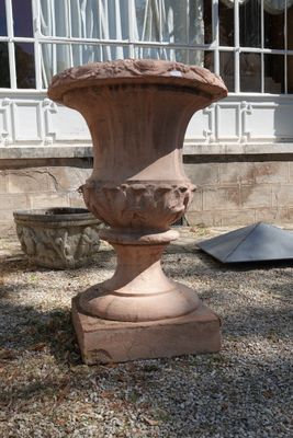 un grand vase en pierre posé sur le gravier devant une maison