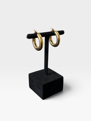 une paire de boucles d'oreilles créoles en or posée sur un présentoir noir