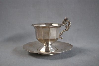 a silver cup and saucer sitting on a saucer