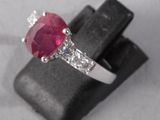 an oval ruby and diamond ring on top of a black piece of wood