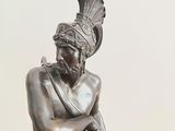 bronze statue of a man with a hat on his head holding a tennis racquet