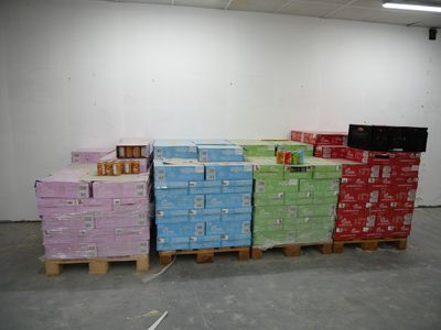Plusieurs piles de cartons sont empilées sur des palettes dans un entrepôt