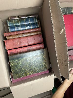 un homme tenant une boîte remplie de livres devant une pile de livres