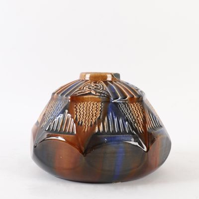 un vase brun et bleu posé sur une surface blanche