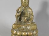 brass statue of a person sitting on a rock with a bird in his hand