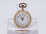 une petite montre de poche en or posée sur un socle transparent