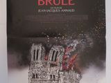 une affiche accrochée au mur d'un immeuble sur laquelle on peut lire « Notre-Dame brûle »