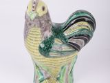 une figurine d'oiseau verte et jaune posée sur une surface blanche