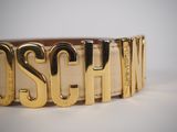 the belt is made of gold metal and has the word moschi on it
