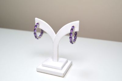 une paire de boucles d'oreilles violettes et blanches posées sur un présentoir blanc