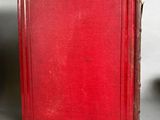 an old red book sitting on top of a table next to a cup