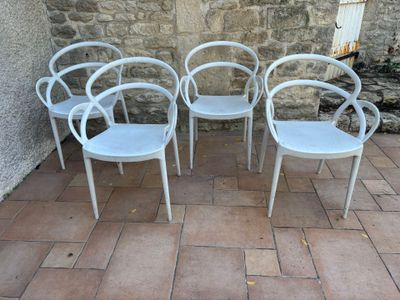four white chairs sitting on a brick patio next to a stone wall